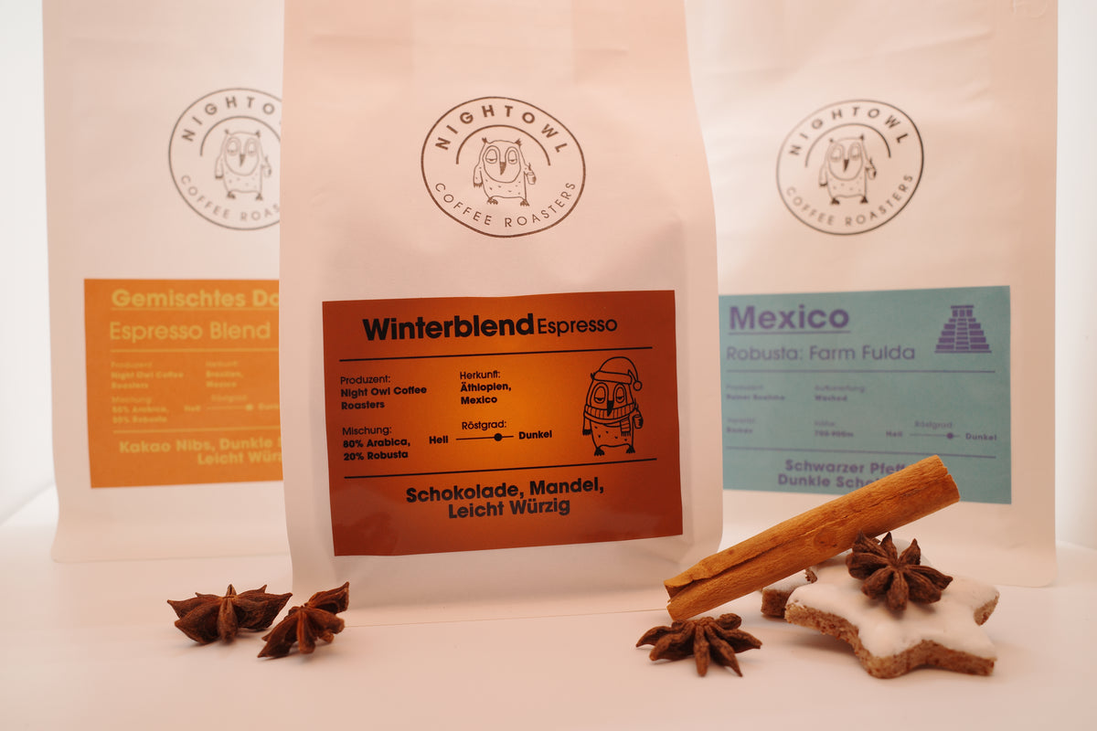 Drei Packungen Kaffee mit Dekoration im Vordergrund.