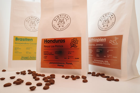 3 Packungen Kaffee mit Bohnen als Dekoration im Vordergrund.